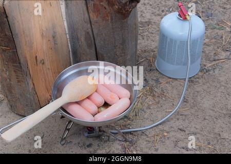 Camping food making. Traveler foods for outdoor activities. Sausages in pot in the forest. Stock Photo