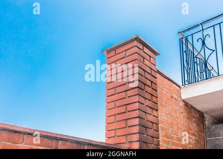 Architectural urban element of a column of red brick near the balcony against the blue sky. Stock Photo