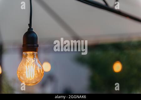Raindrops flow down from the edge of the gazebo close up. a garland of white light bulbs hangs on the ennobled roof of the house. wooden gazebo on the Stock Photo
