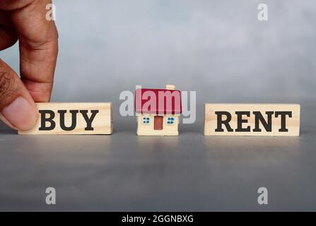 Property, real estate, buy and rent concept. Miniature house and hand pick wooden cube with text BUY over RENT