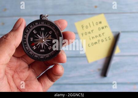 Motivational life quotes. Selective focus image of hand holding compass and text FOLLOW YOUR OWN INNER COMPASS Stock Photo