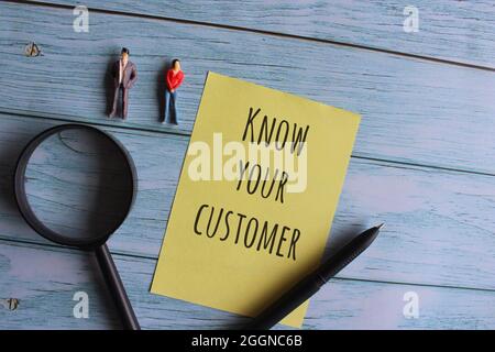 Top view of magnifying glass, miniature people and yellow paper with text KNOW YOUR CUSTOMER on wooden table Stock Photo