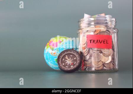 Travel budget concept. Coins in a glass jar, earth globe and compass with copy space for text. Stock Photo