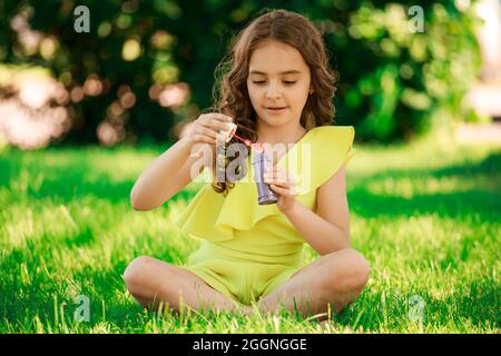 brunette girl with dark hair sits on the grass in the park and blows bubbles. children's portrait. happy childhood. High quality photo Stock Photo