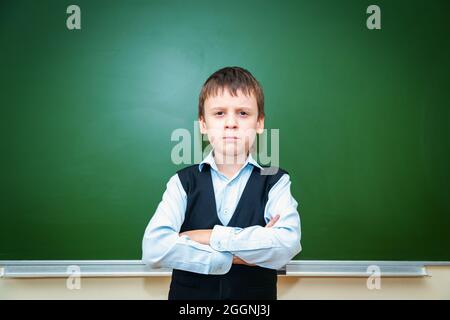 Serious schoolboy near the green school board in the classroom. Elementary school child. Back to school. Stock Photo