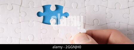Man inserting last piece into white puzzle closeup Stock Photo