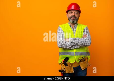 Middle-aged bearded man builder in uniform and hardhat with tools against orange background Stock Photo