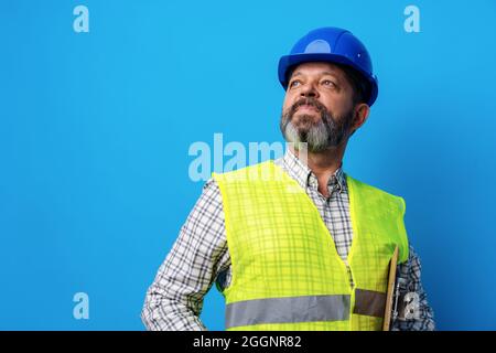 Male builder or handyman in uniform holding clipboard against blue background Stock Photo