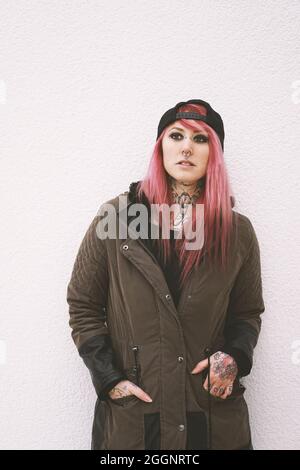 young woman with pink hair piercings and tattoos leaning against wall Stock Photo