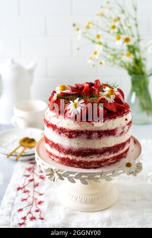 Red velvet cake with strawberry, whipped cream and bouquet of daisies on white board on gray background. Valentines Day, Wedding dessert or Birthday p Stock Photo