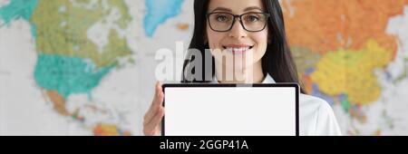 Woman with glasses holding empty digital tablet in hands against background of geographic map of world Stock Photo