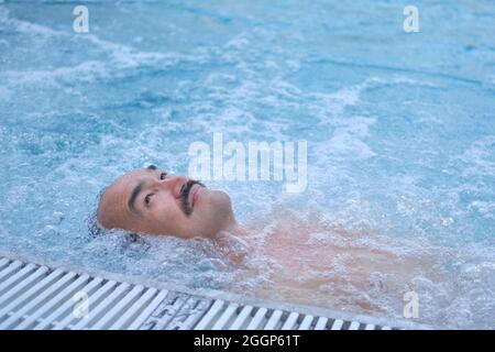 Happy mature asian man laying on water relax in outdoor thermal pool with hydromassage. Stock Photo