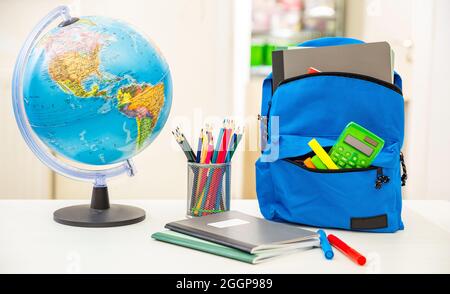 Back to school. Student backpack and supplies on white desk, blur interior room background. Education, study concept Stock Photo