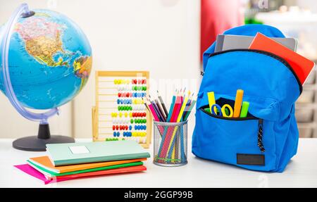 Back to school. Student backpack and supplies on white desk, blur interior room background. Education, study concept Stock Photo