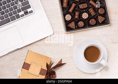 Glass of chocolate milk and variety chocolates  on table with gift box and laptop. Stock Photo