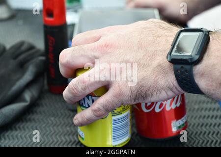 A man picking up two cans of soft drink, Fanta and Coca Cola with a worn watch on his wrist Stock Photo