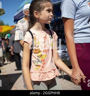 Sokobanja, Serbia, Aug 19, 2021: Portrait of a girl with a lollipop touring a village fair with mom Stock Photo