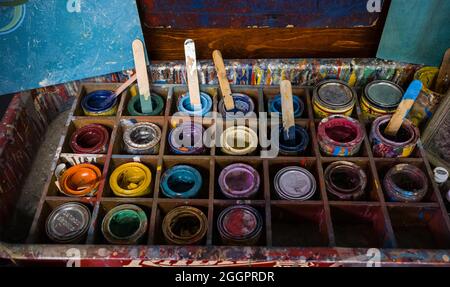 Top view of opened cans of dried up used colorful paints a few with stir sticks and some still closed grouped together in a wooden box with dividers Stock Photo