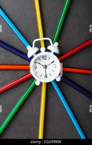 A white alarm clock with colored pencils in the shape of a star. Top view Stock Photo