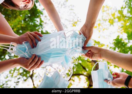 Close up portrait from below of people holding their medical and surgical mask in their hands in the center togetherness, quarantine freedom concept Stock Photo