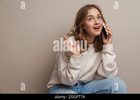 Young happy woman talking on mobile phone and gesturing isolated over grey background Stock Photo