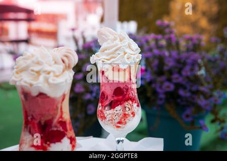 Strawberry ice cream dessert with whipped cream and crushed meringue, served in a glass cup. A cup of coffee on the coffee table. Stock Photo