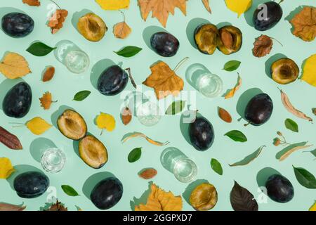 Plums and dried leaves of yellow, green, brown, orange color on a pastel green background. Glasses with brandy. The idea of autumn creative compositio Stock Photo