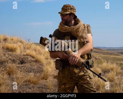 Mercenary sniper in camouflage clothes under the scorching sun. He stands with a rifle and surveys the area. Concept of a professional army during arm Stock Photo