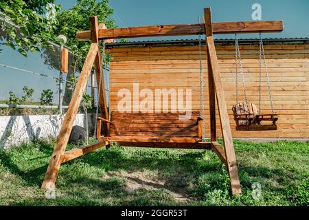 Low angle view of wooden swing seat in garden, in summer with blue sky and green grass Stock Photo