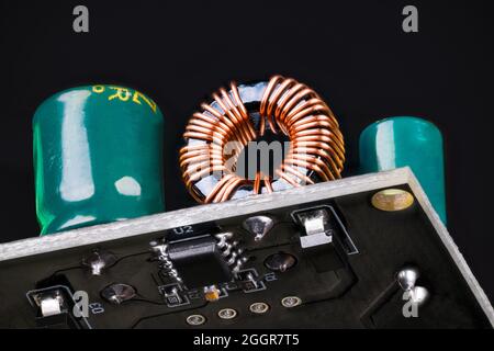 Printed circuit board with toroidal coil or green capacitors on black background. Through-hole technology on PCB upper side or surface mount on bottom. Stock Photo