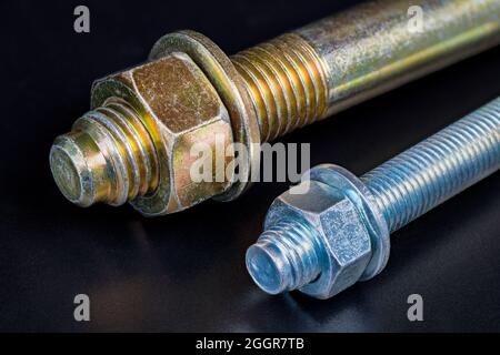 Metal nuts and washers on galvanized bolts detail with reflection on a black background. Ends of two wedge expansion anchors to fixing into concrete. Stock Photo