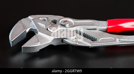Detail of metal adjustable wrench with reflection on a black background. Close-up of steel tongue-and-groove slip-joint pliers in artistic still life. Stock Photo
