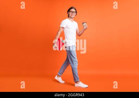 Full body photo of young attractive happy man walk empty space hold note coffee isolated on orange color background Stock Photo