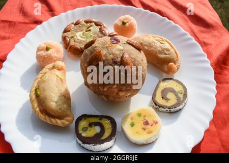 Delicious Indian Assorted sweets like Gujiya, Soan halwa, Barfi and Laddu with orange shaped coconut pudding. Assortment of sweet items served during Stock Photo