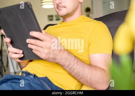 Man using tablet for video conversation while relaxing on couch. Young man working at home Stock Photo