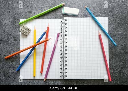 Flat lay of a blank open spiral notebook with copy space, colored crayons, sharpener and eraser for creative work, study or school on a gray table, hi Stock Photo