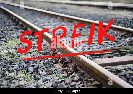 German text Streik (meaning strike) over rusty metal railway tracks and brackets in a ballast bed, selected focus, narrow depth of field Stock Photo