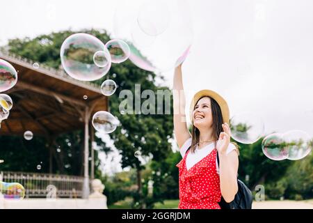 Young hispanic woman having fun while playing with soap bubbles in city park Stock Photo