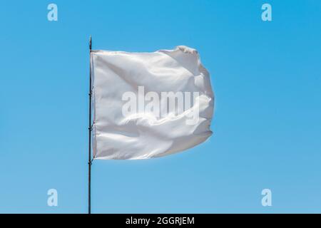 White flag sign and symbol of goodness and truce on blue sky background. Stock Photo