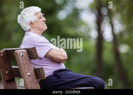 Pensive senior man sitting on bench in summer park Stock Photo