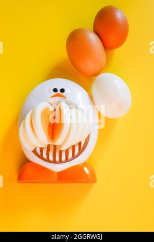 Funny egg slicer with hard boiled eggs whole ,  peeled and sliced on a yellow background Stock Photo