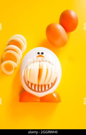 Funny egg slicer with hard boiled eggs whole ,  peeled and sliced on a yellow background Stock Photo