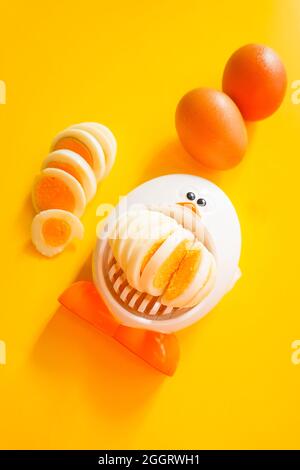 Funny egg slicer with hard boiled eggs whole ,  peeled and sliced on a yellow background Stock Photo