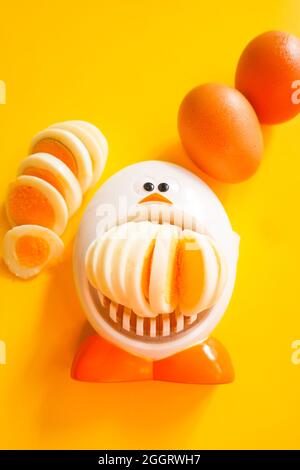 Funny egg slicer with hard boiled eggs whole ,  peeled and sliced on a yellow background Stock Photo