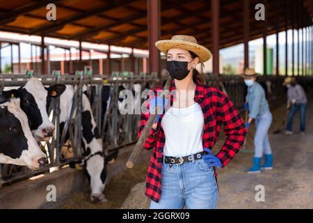 Confident young female farmer in mask standing in cowshed Stock Photo
