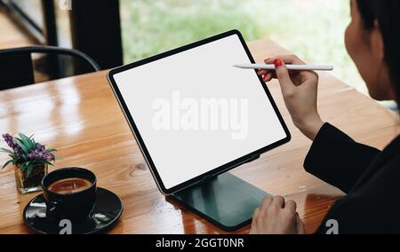 Side view of female freelancer holding stylus pen pointing on screen of digital tablet with blank white screen Stock Photo