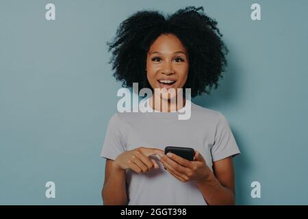 Beautiful happy dark skinned girl holding modern smartphone and chatting with friend online