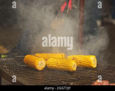 Fresh corn on the grill grate and a big cloud of smoke in the background.