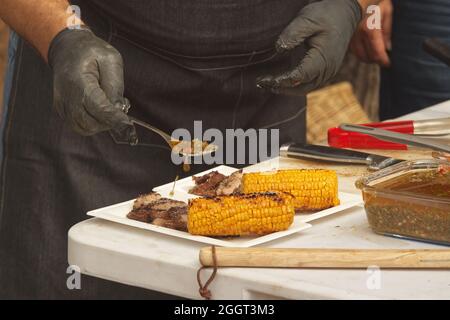 Chef prepares paper trays with grilled food, meat and corn for customers Stock Photo