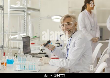 Portrait of senior scientist working with microscope, laptop and lab equipment Stock Photo